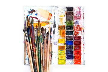 Fototapeta premium Used water-color paint-box and dirty artist paint brushes. Top view. Isolated image with space for your text