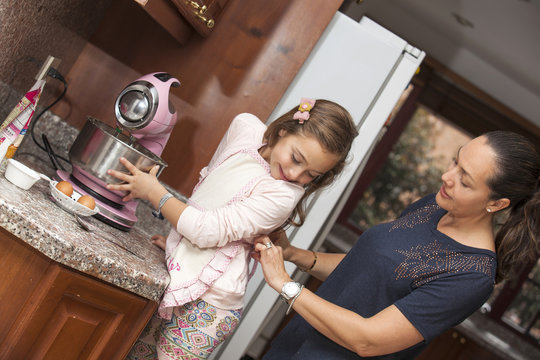 Mam&aacute; poni&eacute;ndole el delantal a la hija para cocinar juntas