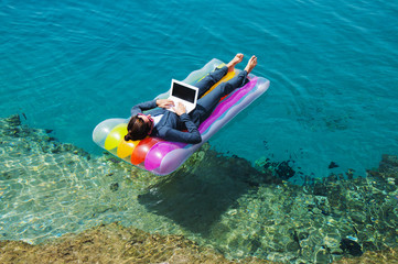 Happy businesswoman with laptop on floating mattress in red sea  