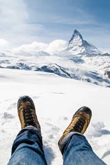 Tableaux sur verre Cervin Men's legs in the trekking boots lying on the snow with the background of Matterhorn, Switzerland.