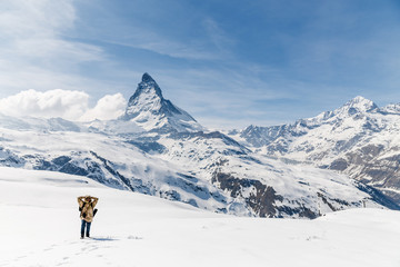 A man putting his hands on head standing on the snow in the background of Matterhorn.