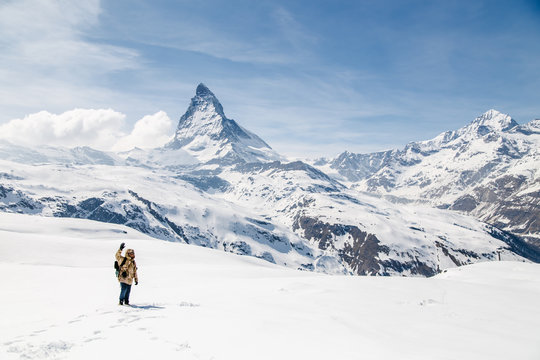 A man waving his hand standing on the snow in the background of Matterhorn.