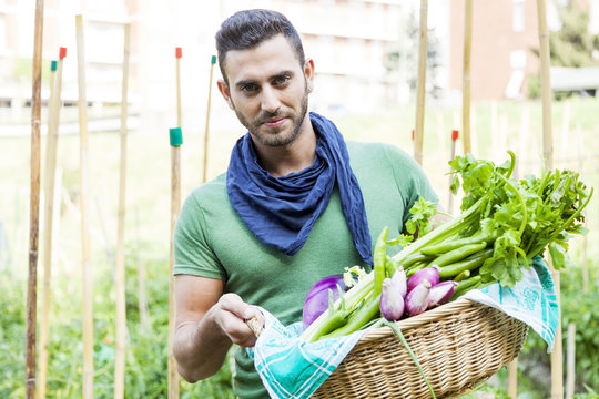 young farmer showing a basket of vegetables in his garden