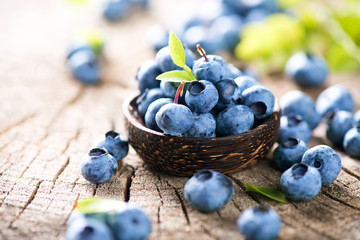 Juicy and fresh blueberries with green leaves in wooden bowl - obrazy, fototapety, plakaty