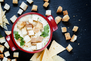 Cheese soup with croutons in red portioned saucepan, top view