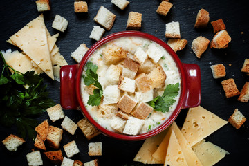 Cheese soup with croutons in red portioned saucepan, top view