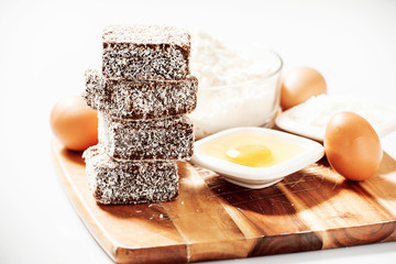 Fototapeta premium Group of Lamingtons on a timber cutting board with food ingredients in the background 