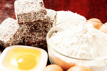 Group of Lamingtons on a timber cutting board with food ingredients in the background 