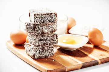 Group of Lamingtons on a timber cutting board with food ingredients in the background 