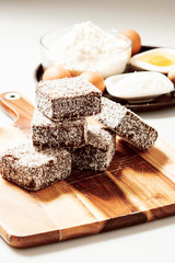 Group of Lamingtons on a timber cutting board with food ingredients in the background 