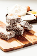 Group of Lamingtons on a timber cutting board with food ingredients in the background 