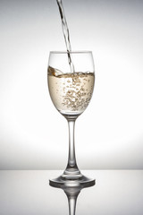 White wine pouring into wineglass on white background