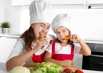 happy mother and little daughter in apron and cook hat eating carrots together 