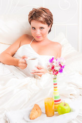 Obraz na płótnie Canvas Lovely woman drinks coffe while sits in bed