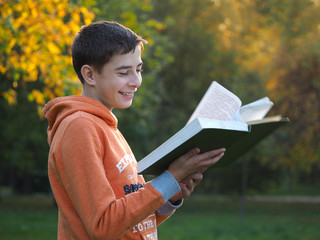 Мальчик читает книгу и улыбается. Осень, парк, солнце. Хорошее настроение, теплая погода. Позитивная фотография