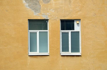 Два окна с вставленным новыми пластиковыми рамами на фоне старой желтой частично облупившейся стены