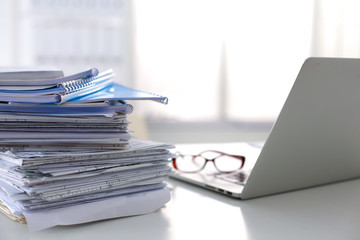 Laptop with stack of folders on table on white background