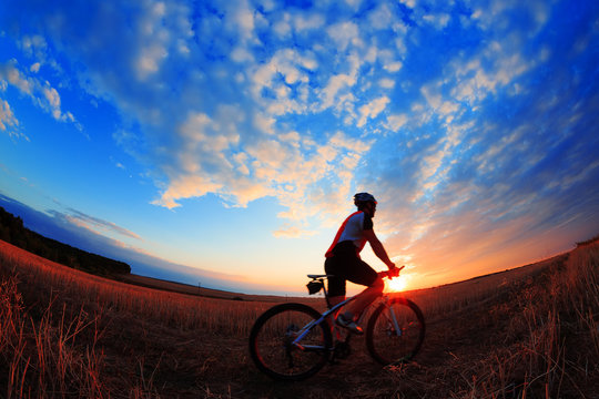 Silhouette Of A Biker And Bicycle On Sunset Background.