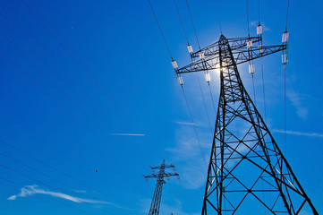 Strommast mit Sonne vor blauem Himmel