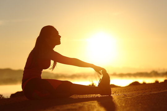 Silhouette of a fitness woman stretching at sunset