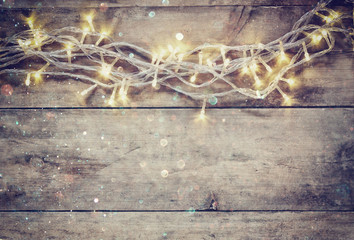Christmas warm gold garland lights on wooden rustic background. filtered image with glitter overlay

