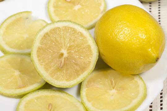 Half lemon and slices beside a full lemon in white dish