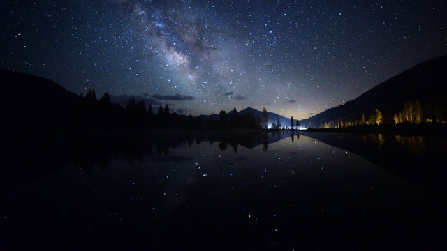 Astrophotography time lapse footage with tilt up motion of milky way galaxy spanning over reflective alpine lake in Yosemite National Park, California