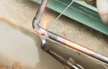 Plumbing contractor works sweating the joints on the copper pipe domestic water system on a luxury...