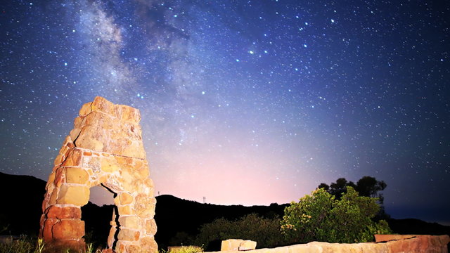  Astrophotography time lapse footage with zoom out motion of milky way galaxy spanning over arch-shaped abandoned brick ruin structure at Knapp's Castle in Santa Barbala, California