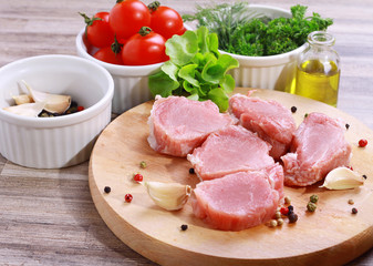 Fresh raw pork fillet medallions with salad, olive oil and cherry tomatoes on wooden cutting board. Healthy lifestyle