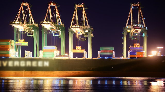 Time lapse footage with pan left motion of industrial cranes loading containers onto container ship at port of Los Angeles at night