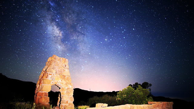  Astrophotography time lapse footage with tilt down motion of milky way galaxy spanning over arch-shaped abandoned brick ruin structure at Knapp's Castle in Santa Barbala, California