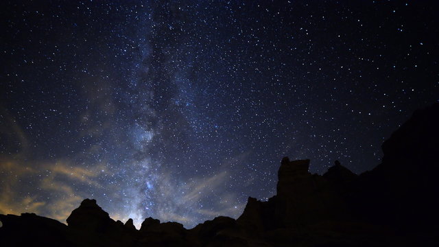 Astrophotography time lapse footage with pan left motion of Milky Way galaxy spanning across rugged sandstone formation in Mojave Desert at Red Rock Canyon State Park, California