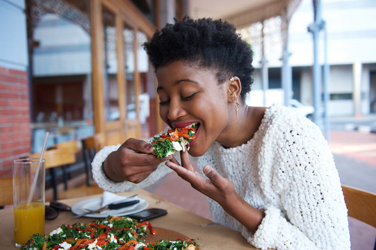 African american woman eating pizza at outdoor restaurant