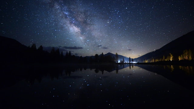 Astrophotography time lapse footage with zoom in motion of milky way galaxy spanning over reflective alpine lake in Yosemite National Park, California
