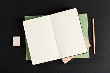 Open blank notepad with empty white pages laying above book with pencil on black background. ideal for text