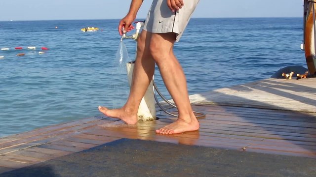 Man washes feet from sand under water stream on the deck