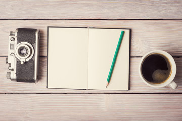 Retro camera, open notebook and cup of coffee on rustic wooden b