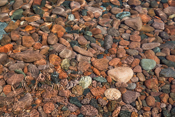 Colorful, smooth stones lie under ripples of water near the shor