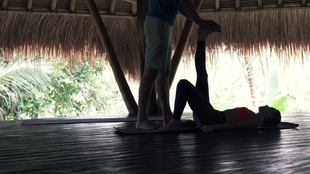 Personal trainer helping young woman stretch leg in wooden barn
