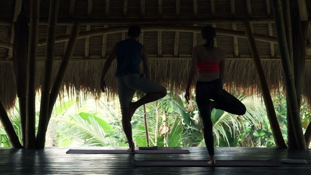 Young couple exercising yoga, doing balance pose in wooden barn
