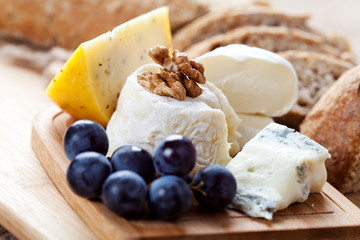 Cheese platter: variety of cheeses on wooden plate with fruits and bread