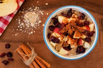 Bowl of autumn inspired oatmeal with apples and cranberries, overhead scene on a wood background