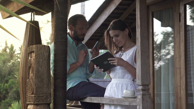 Young couple using smartphone and tablet computer on terrace
