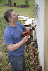 Man working construction job holding drill wearing blue shirt