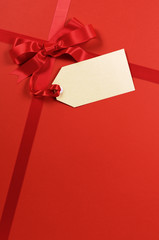 Red gift bow and ribbon for christmas birthday with gift tag on a wrapping paper present background photo vertical