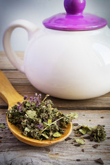 Dry herb tea in a wooden spoon and white teapot