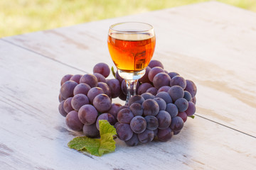 Grapes with leaf and glass of wine on wooden table in garden