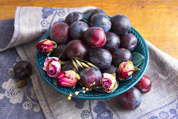 Purple plums in a green plate on a wooden table