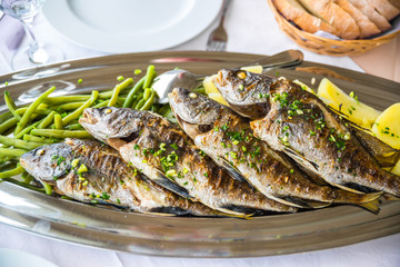 Four grilled fish on a plate with potatoes and vegetables in the Mediterranean region